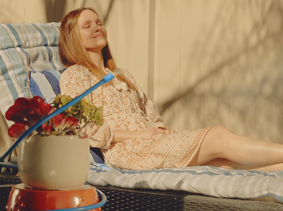A woman lounging in chair outside with Arctic Air® Personal Mister misting the space around her